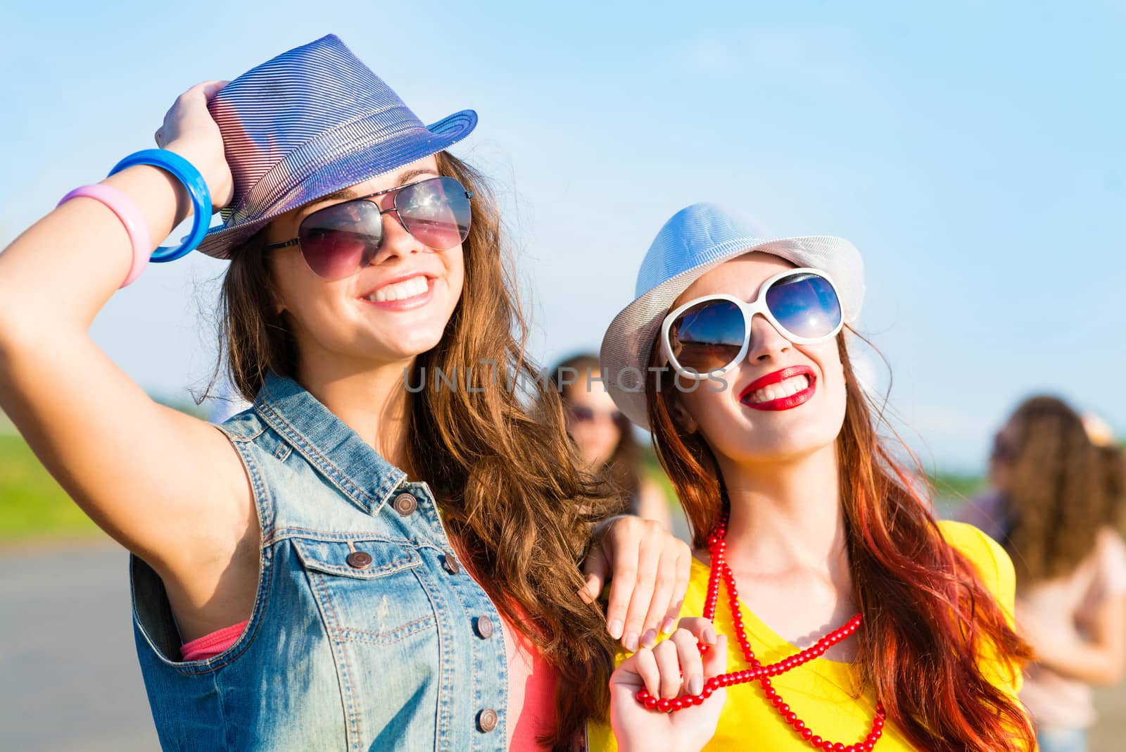 Two young girlfriends having fun on the background of blue sky and friends