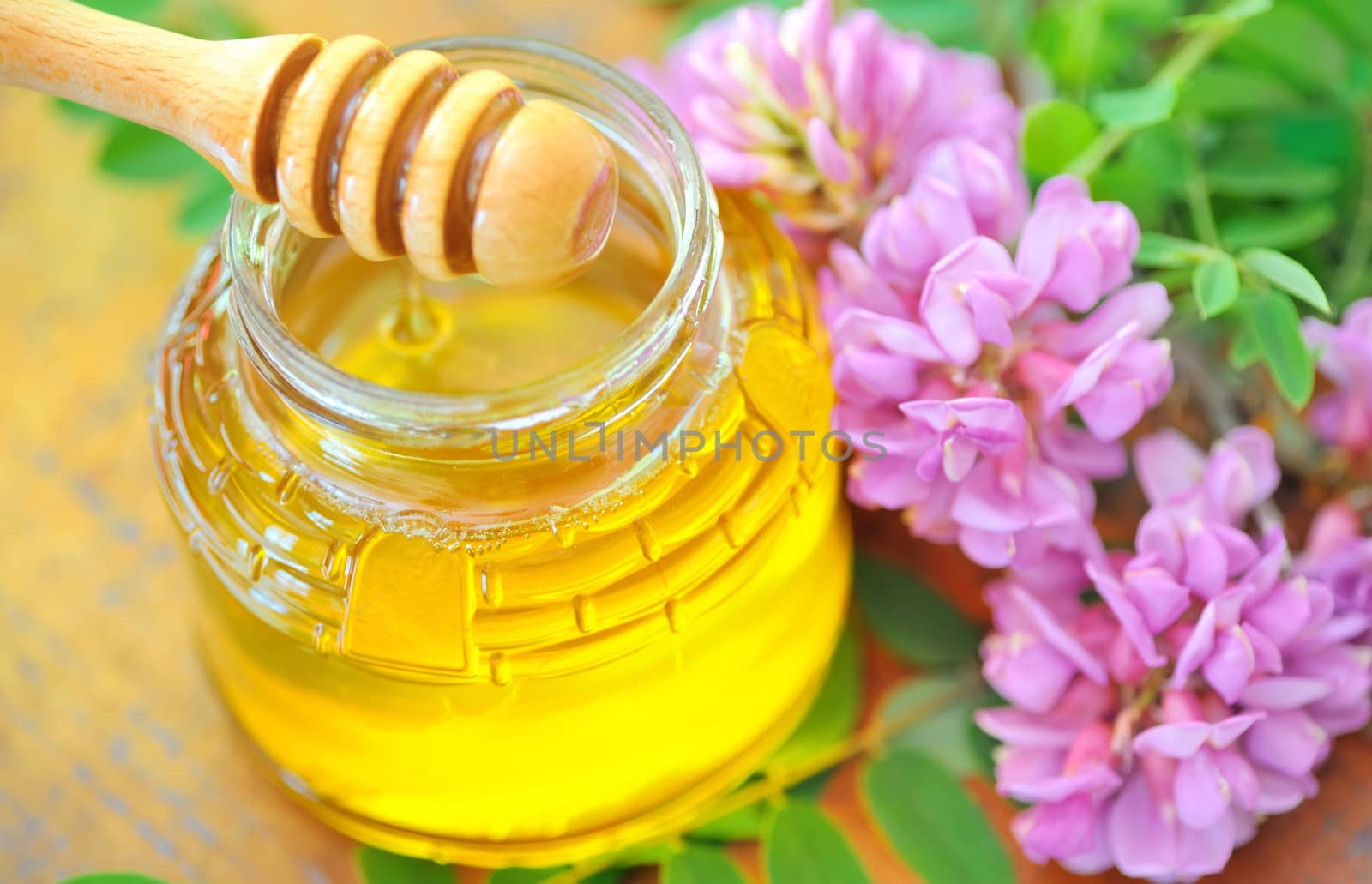 glass jar full of honey and stick with acacia pink and white flowers
