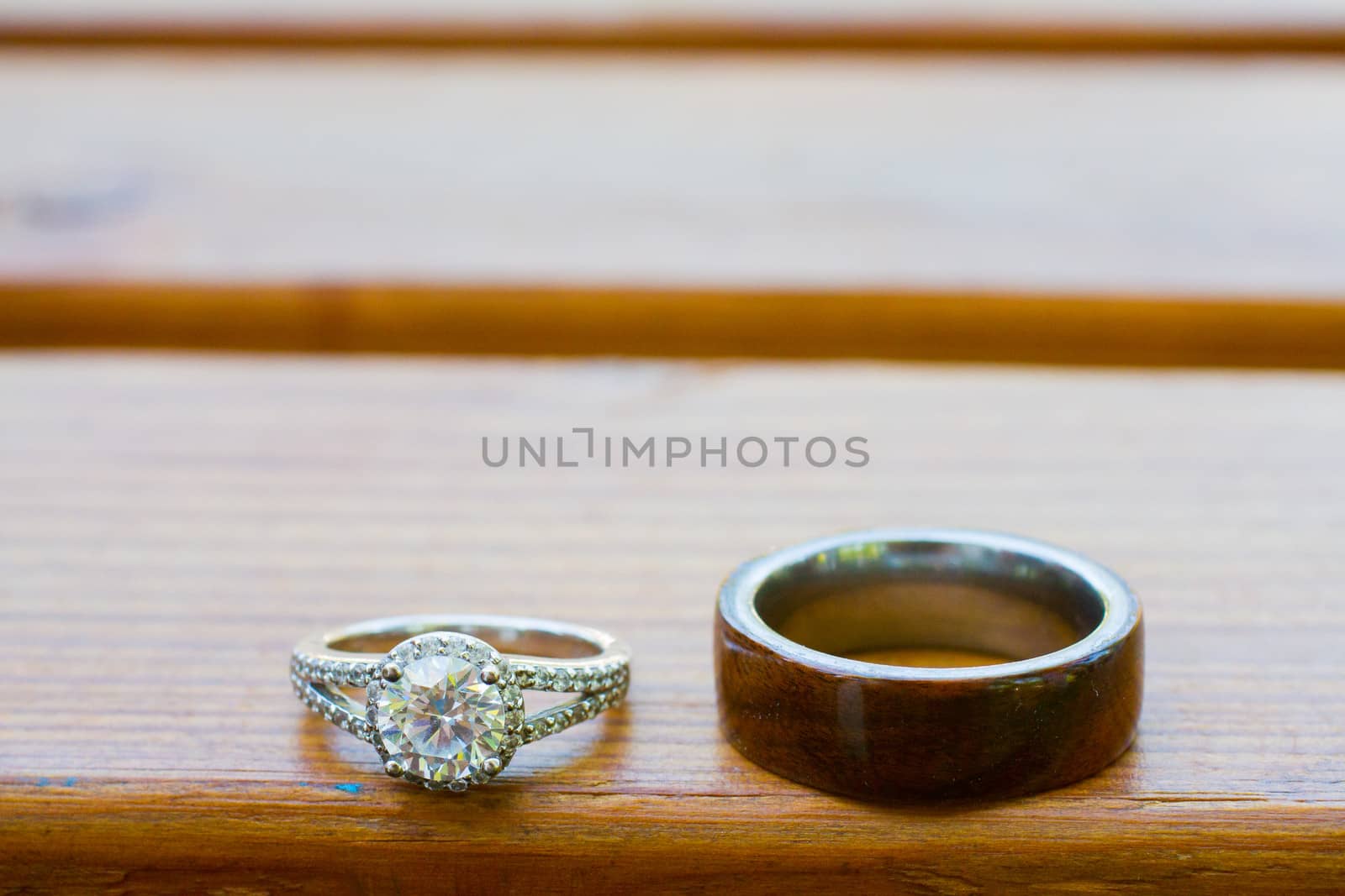 The rings of a bride and groom are photographed on a wooden bench.