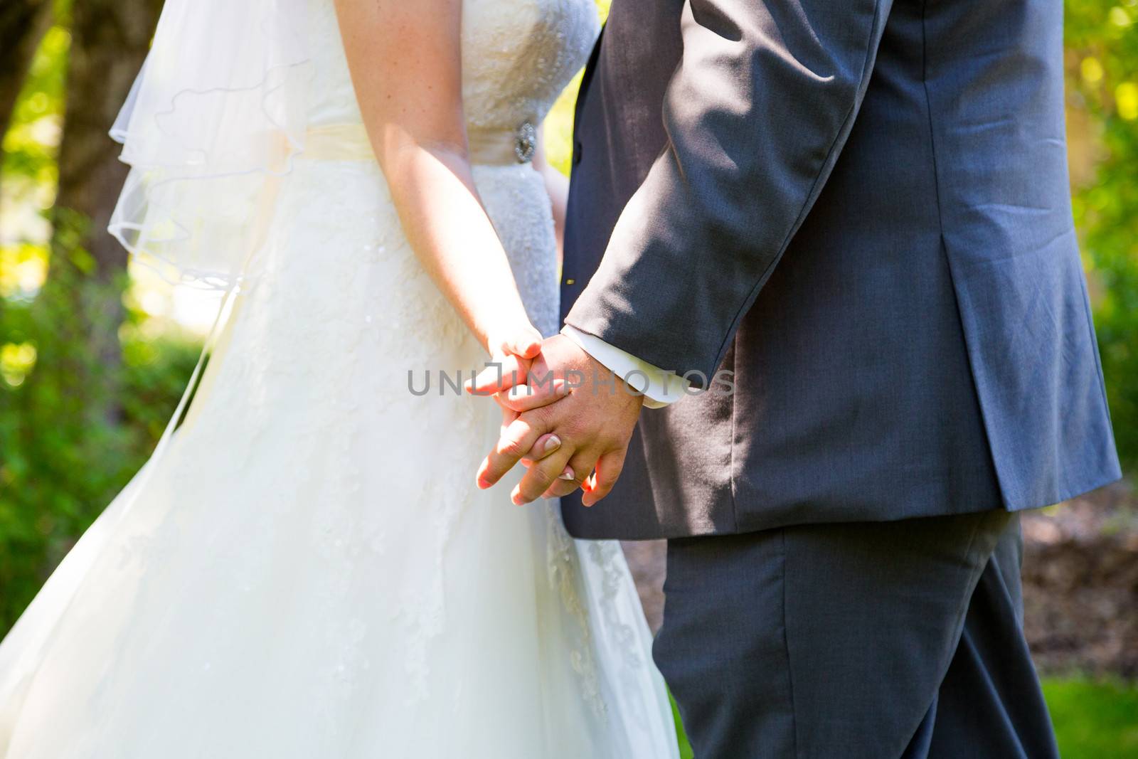 This bride and groom hold hands romantically while kissing on their wedding day.