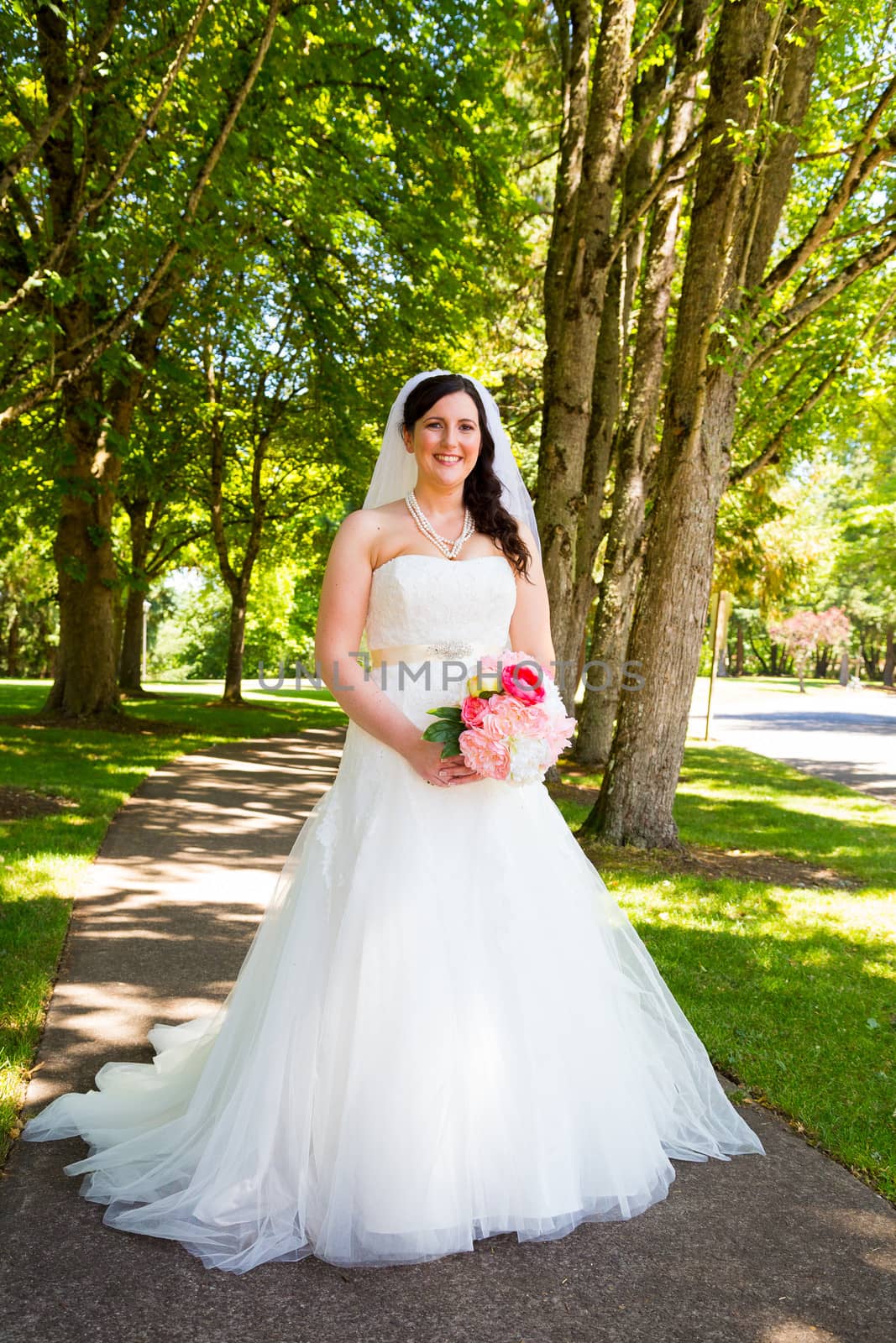 A bride poses for some portraits while wearing her wedding dress at a park outdoors just before here wedding ceremony.