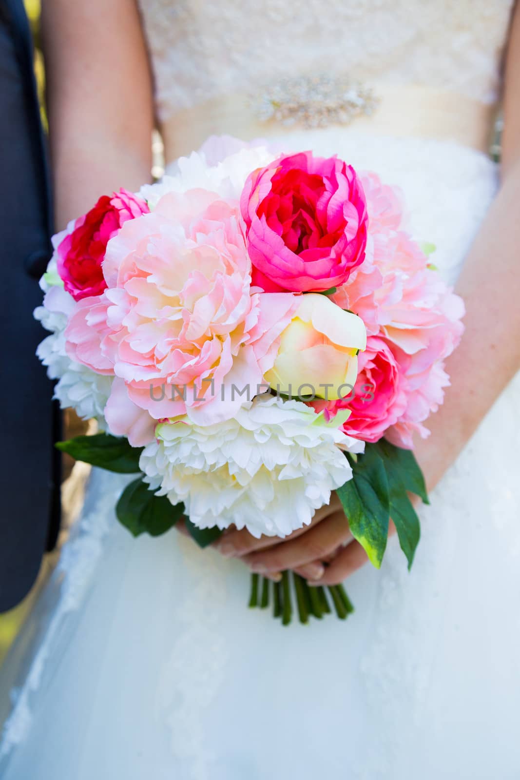 This bride holds her bouquet of white and pink flowers against her white wedding dress.