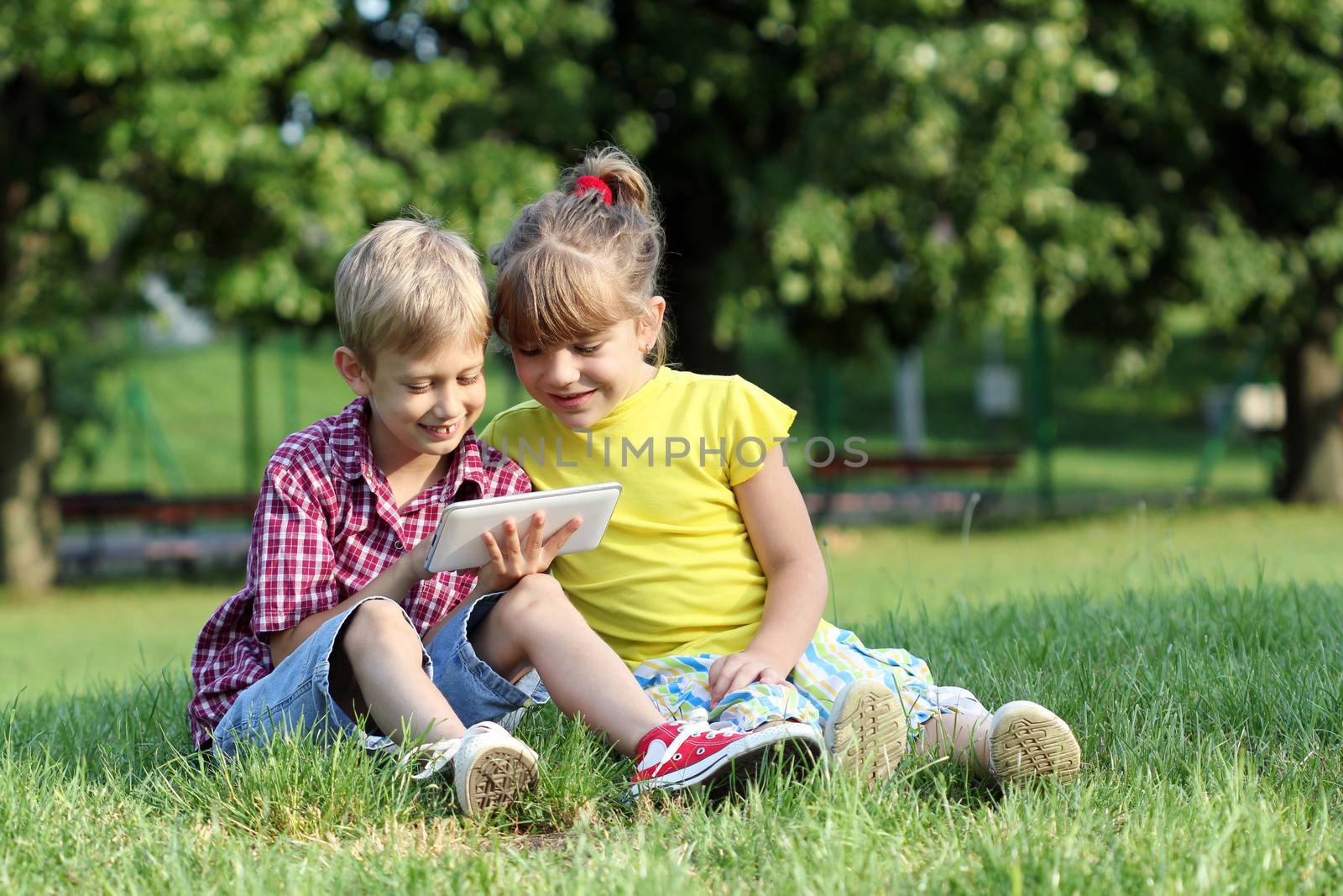 boy and little girl play with tablet pc in park