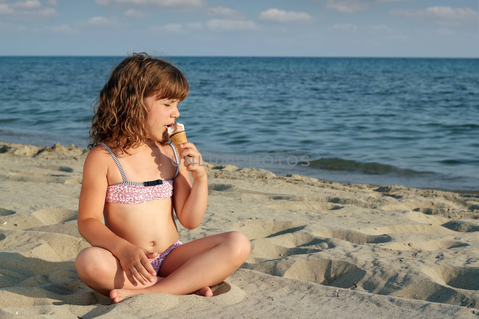 little girl sitting on beach and eat ice cream