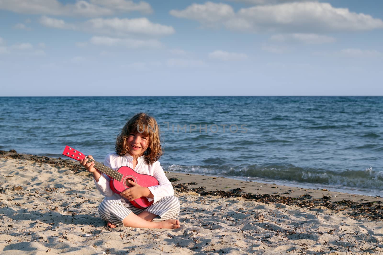 little girl sitting on beach and play guitar by goce