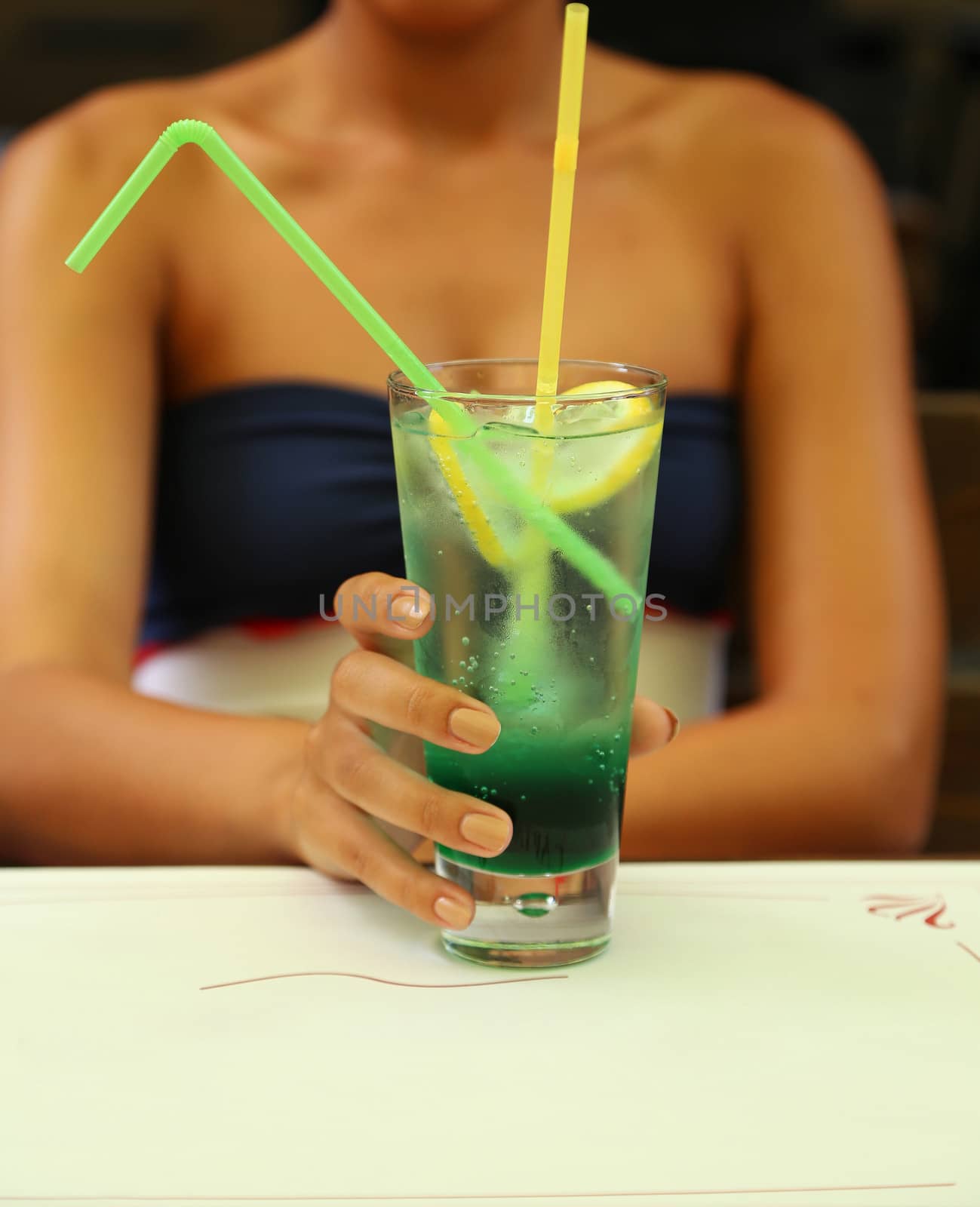 Green alcoholic cocktail in a tall glass against woman trunk