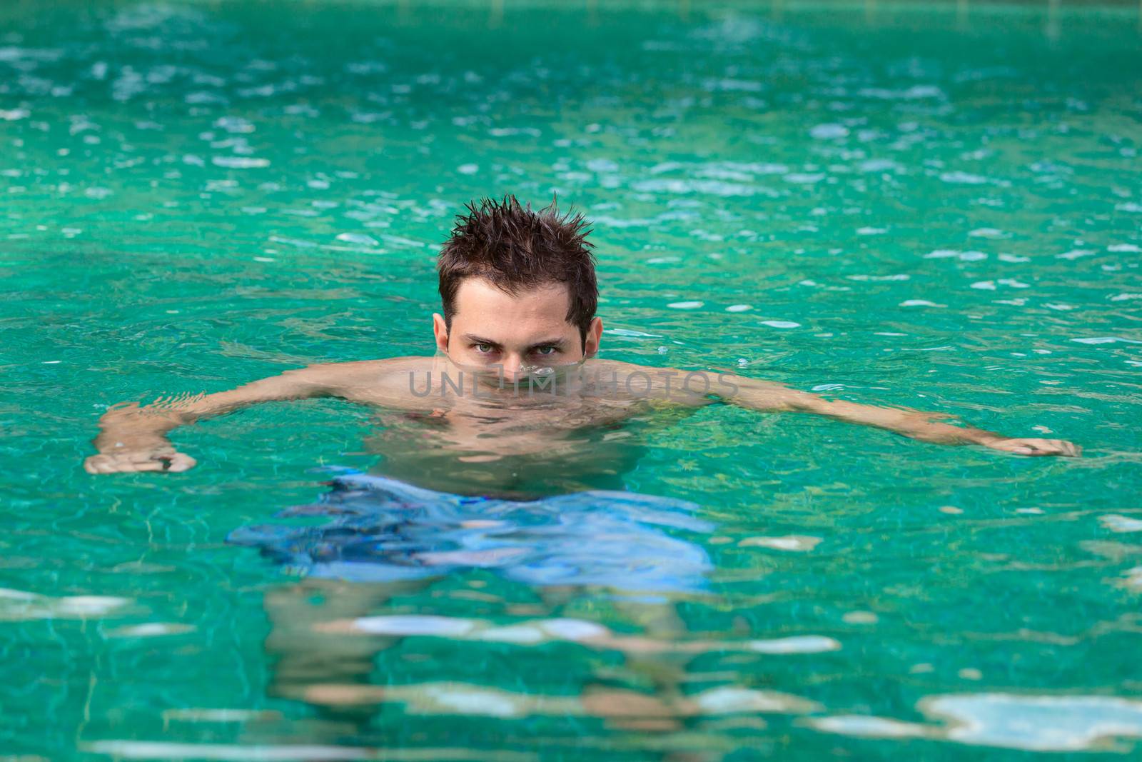 Young serious man looking from water in the swimming pool 