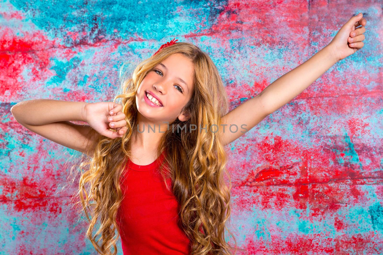 Blond happy kid girl in red happy with arms up in grunge background