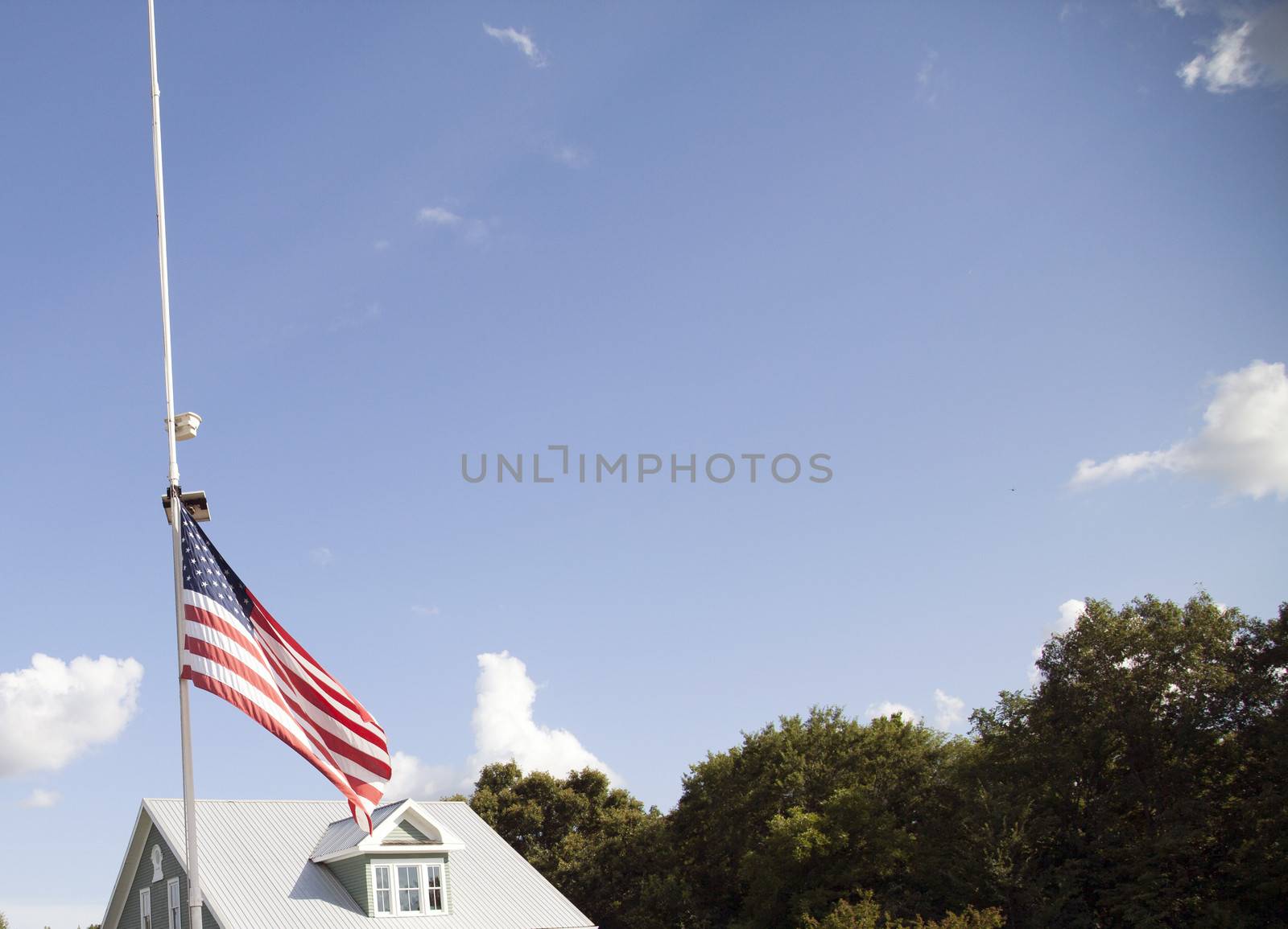 American flag at half mast with top of house and tree tops in the background