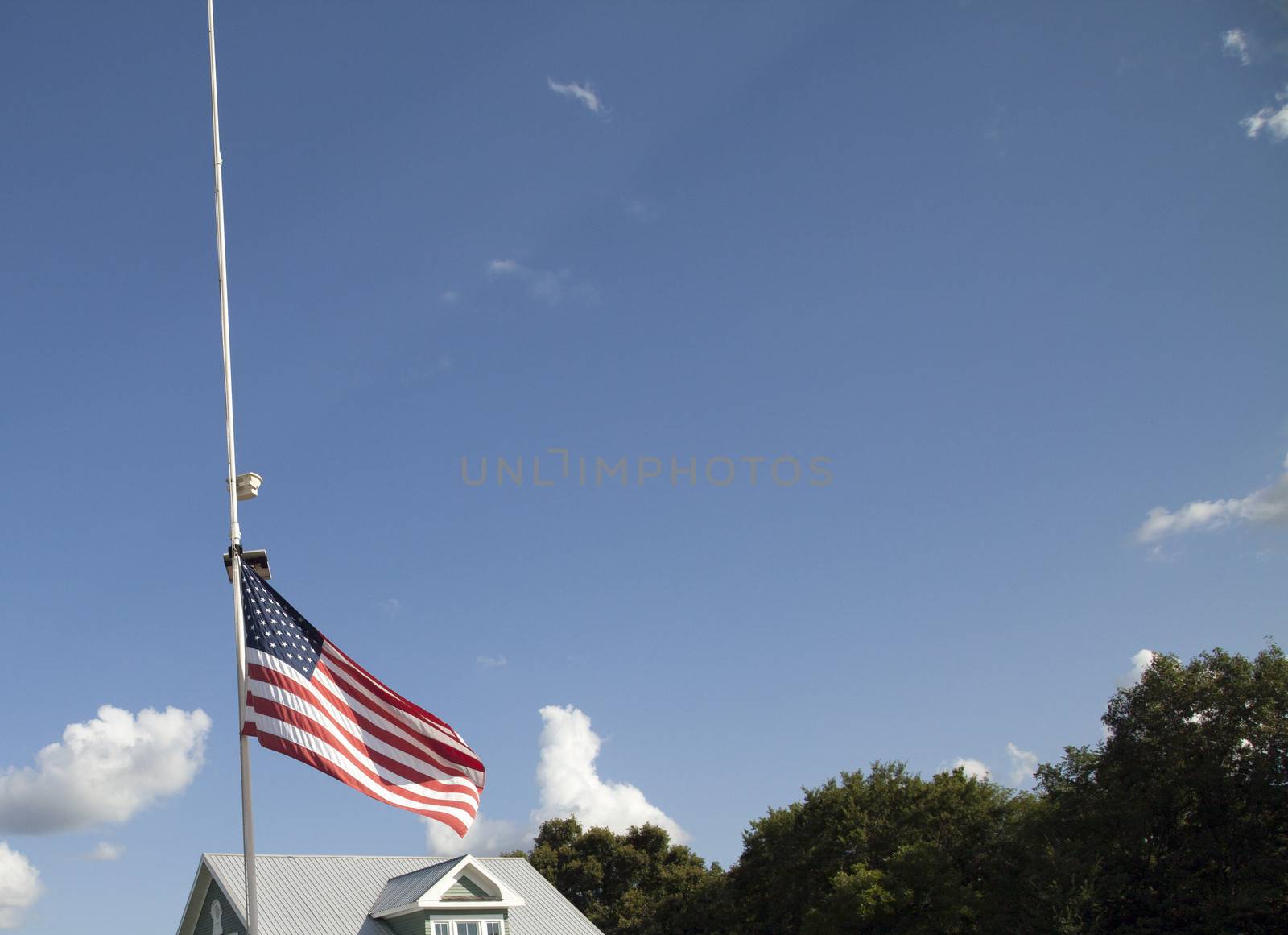 American flag at half mast with top of house and tree tops in the background
