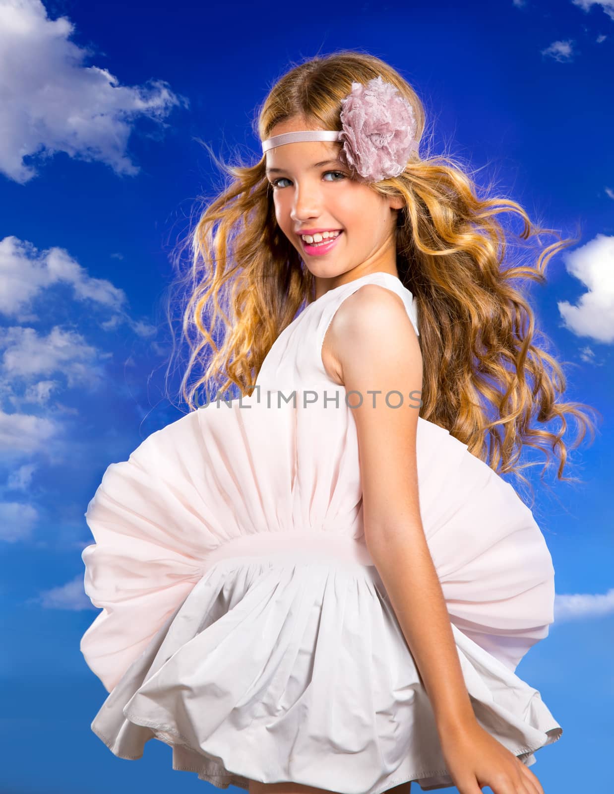 Blond happy girl with fashion dress and wind blowing hair in a blue sky background