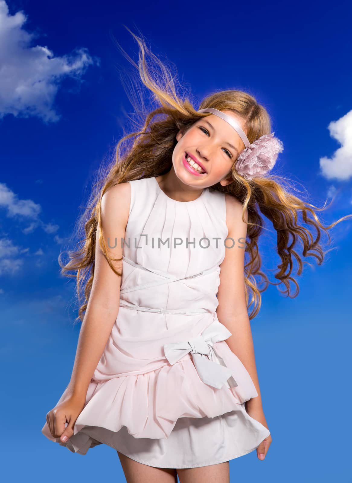 Blond happy girl with fashion dress and wind blowing hair in a blue sky background