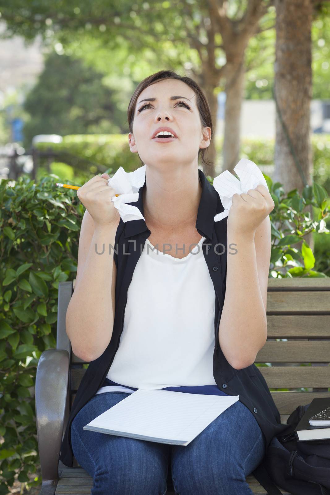 Frustrated and Upset Young Woman with Pencil and Crumpled Paper in Her Hands Sitting on Bench Outside.