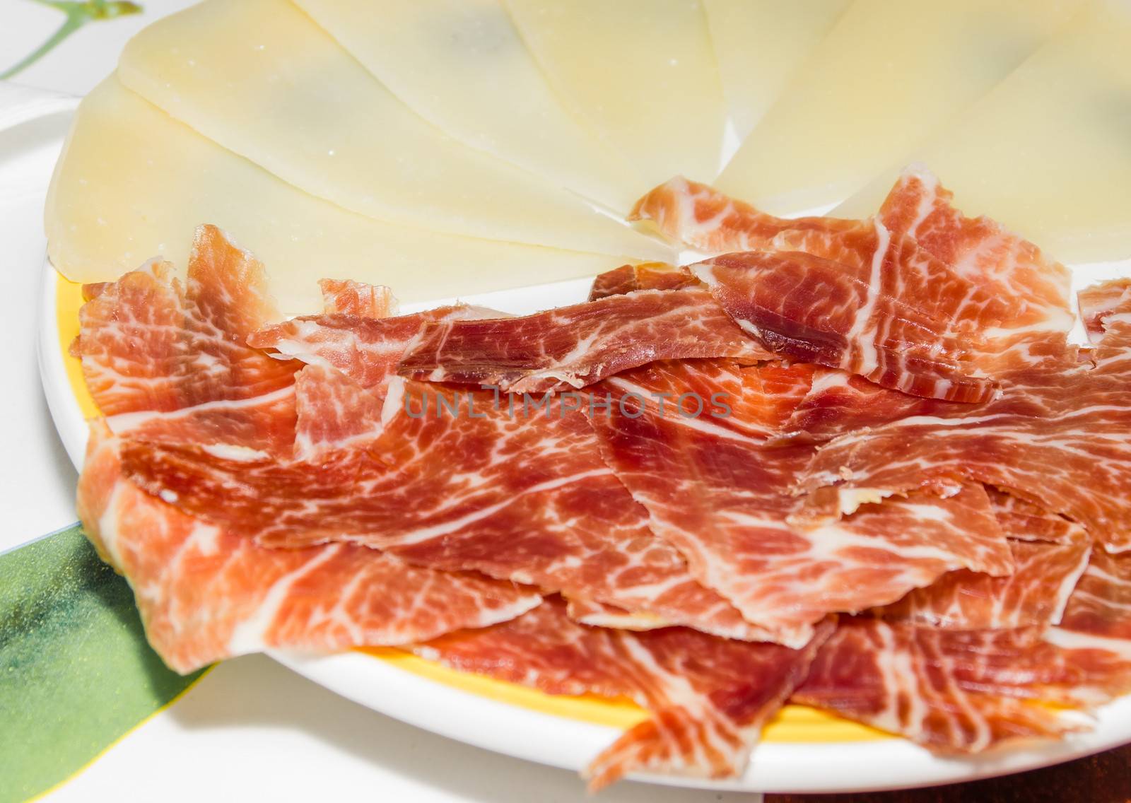 Closeup of typical spanish tapa, with slices of serrano ham and manchego cheese served in a plate