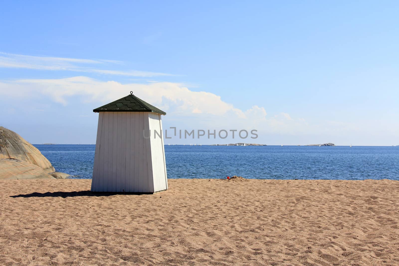 Wooden beach hut facing the blue sea and ships on the horizon in Hanko, Finland.