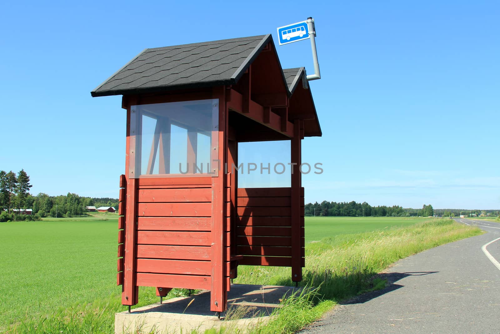 Rural bus stop shelter made of wood and painted red by highway on a sunny day at summer. Space for your advertisement.