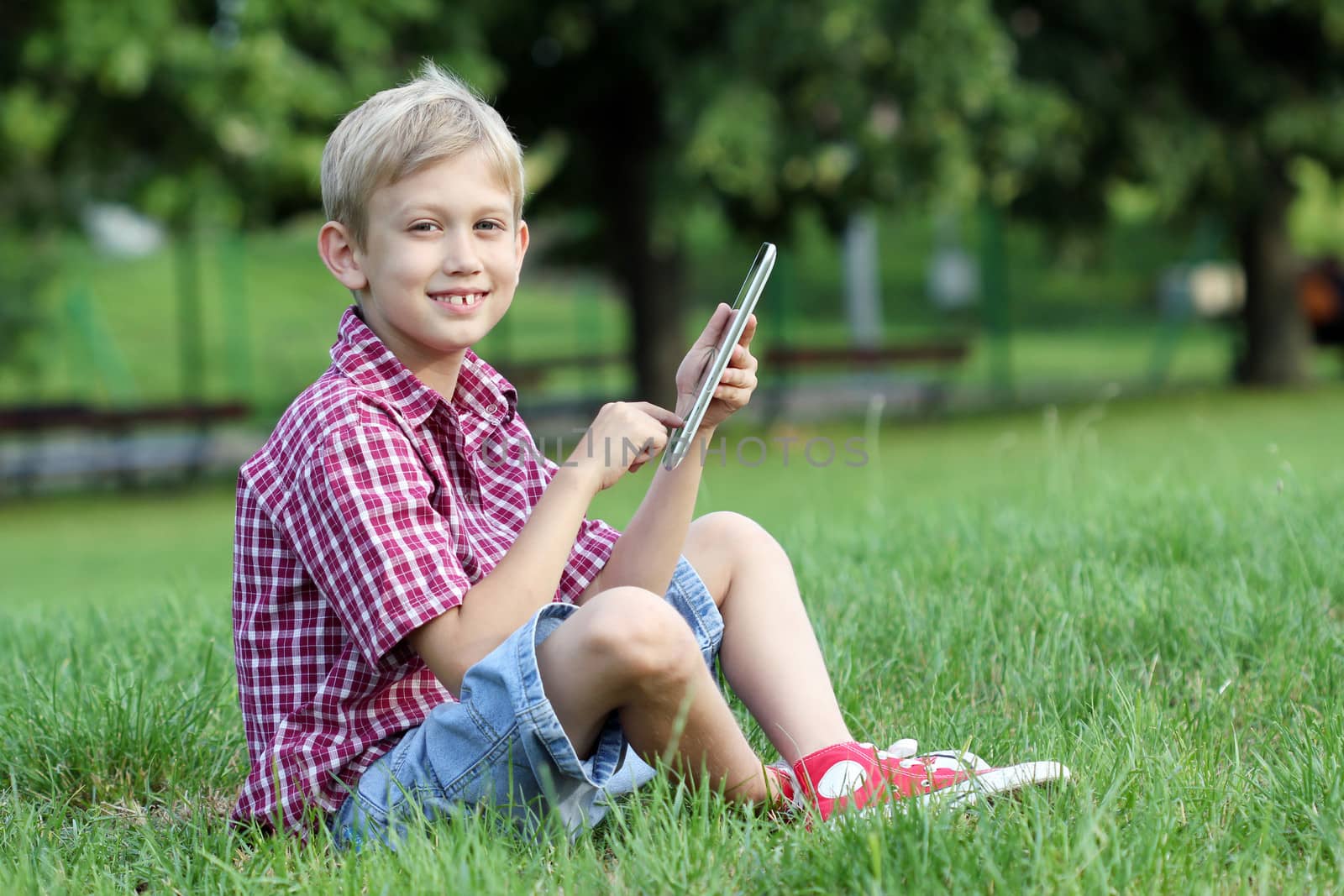 happy boy play with tablet pc in park by goce