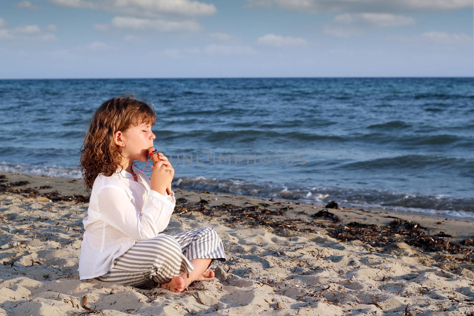 little girl play pan pipe on beach by goce