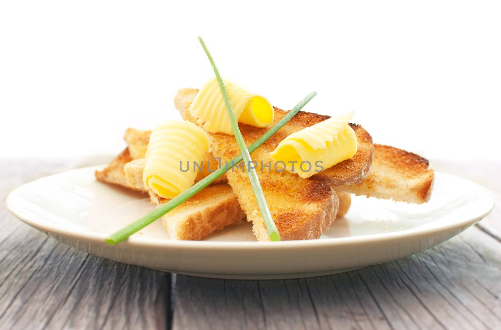 Slices of toasted bread with butter curls and chives on a plate