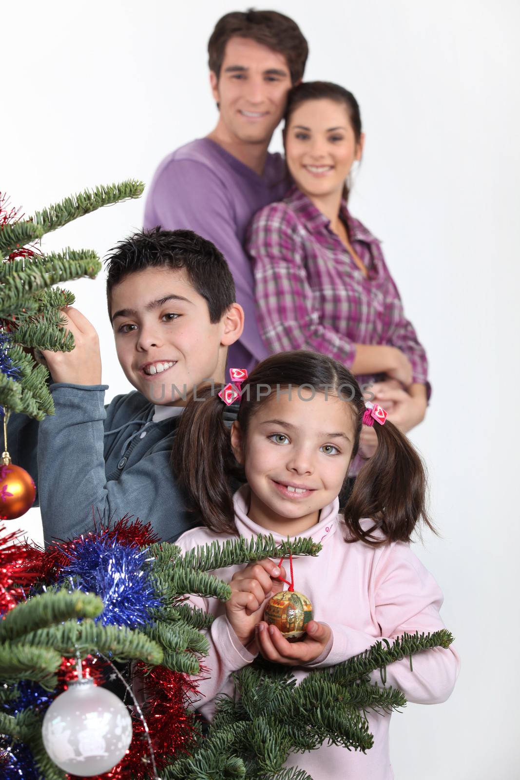 happy parents with children decorating Christmas tree by phovoir