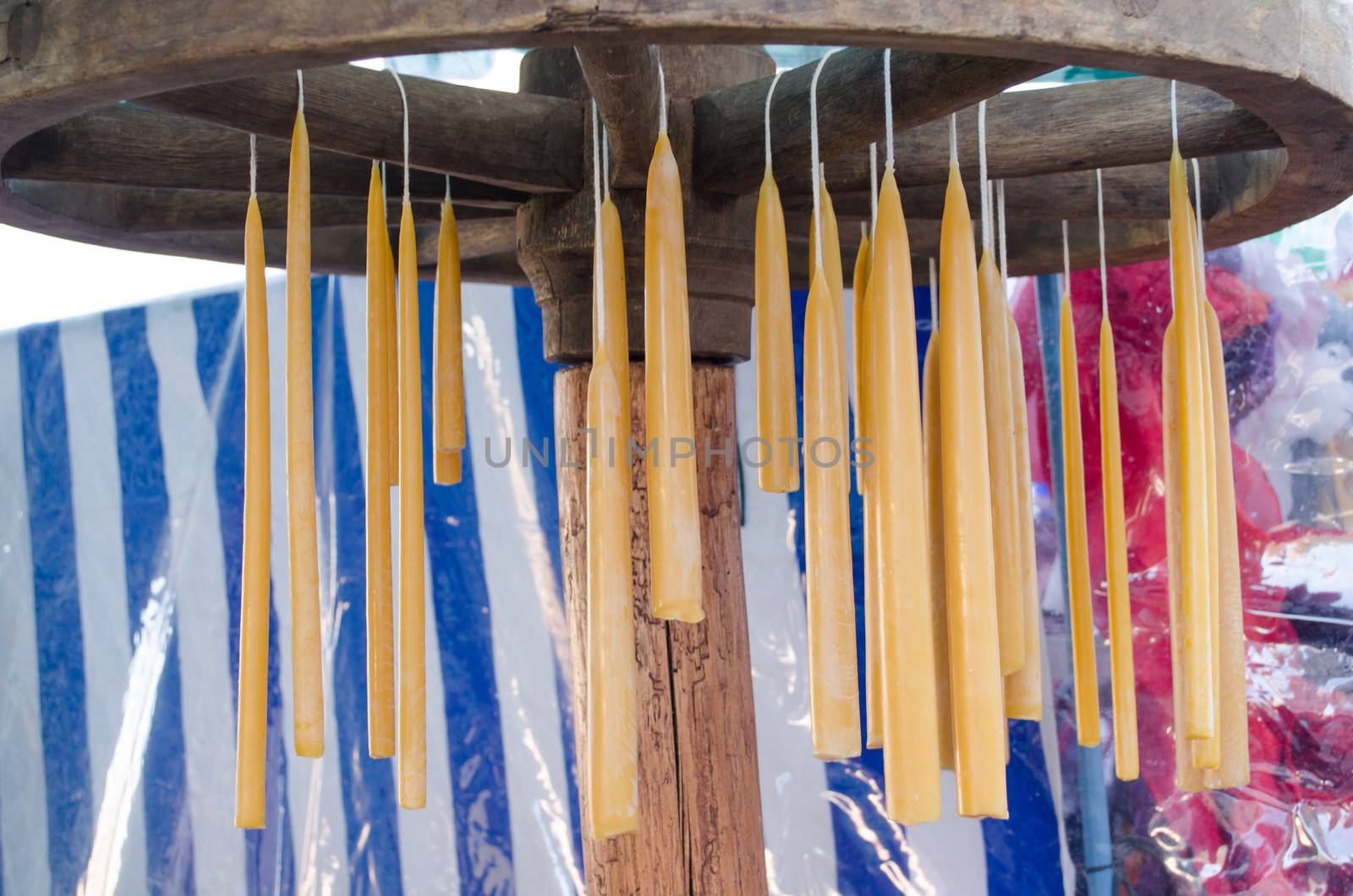 handmade hand dip yellow wax candles hang on retro wheel. traditional rural crafts.