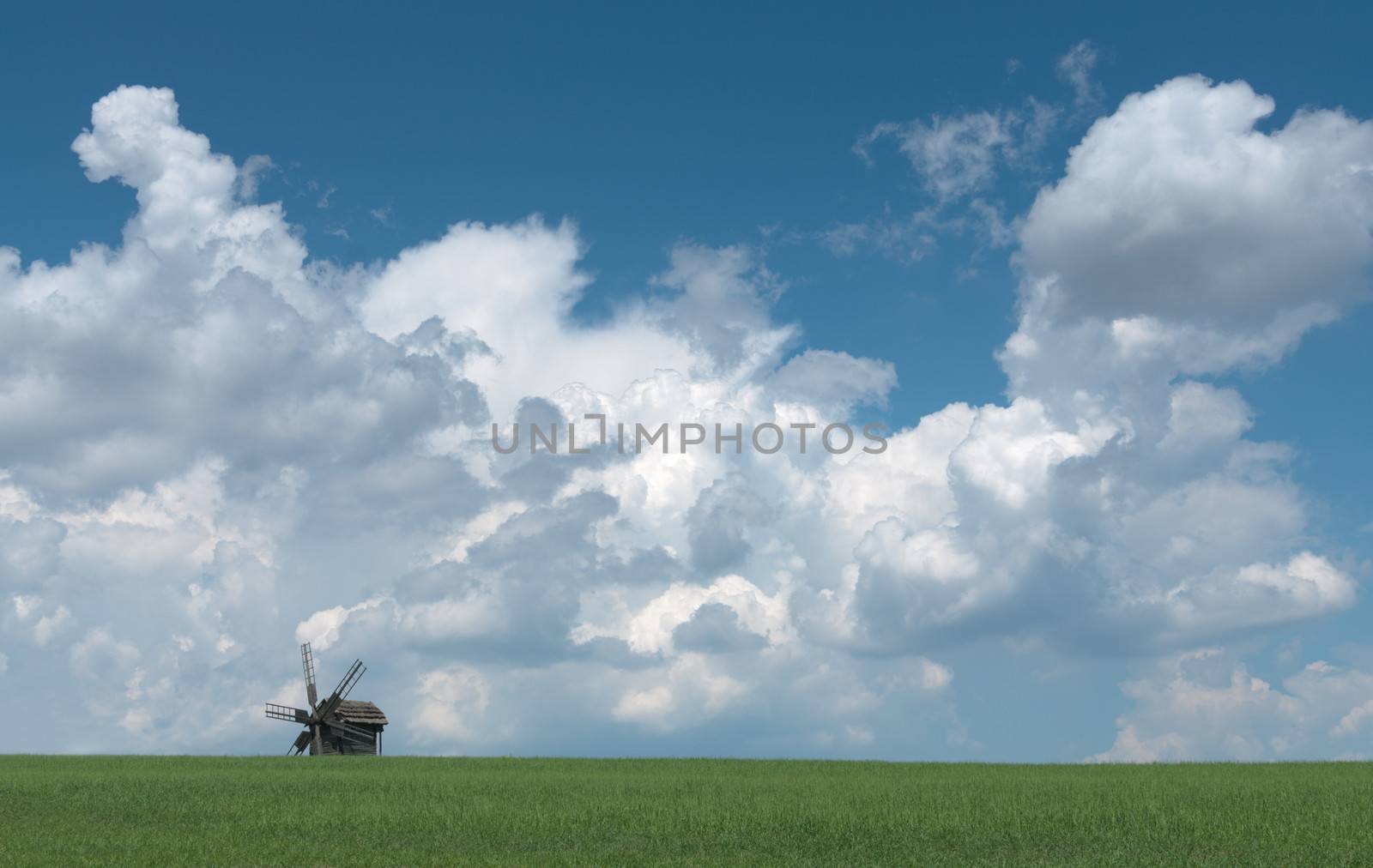 Old wooden windmill against sky with clouds.
