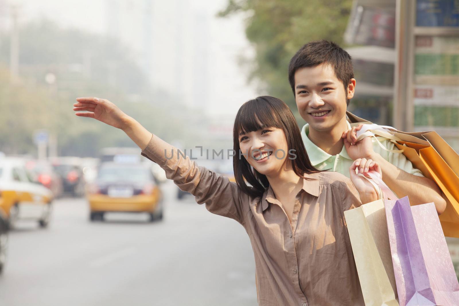 Young couple with shopping bags hailing a taxicab in Beijing by XiXinXing