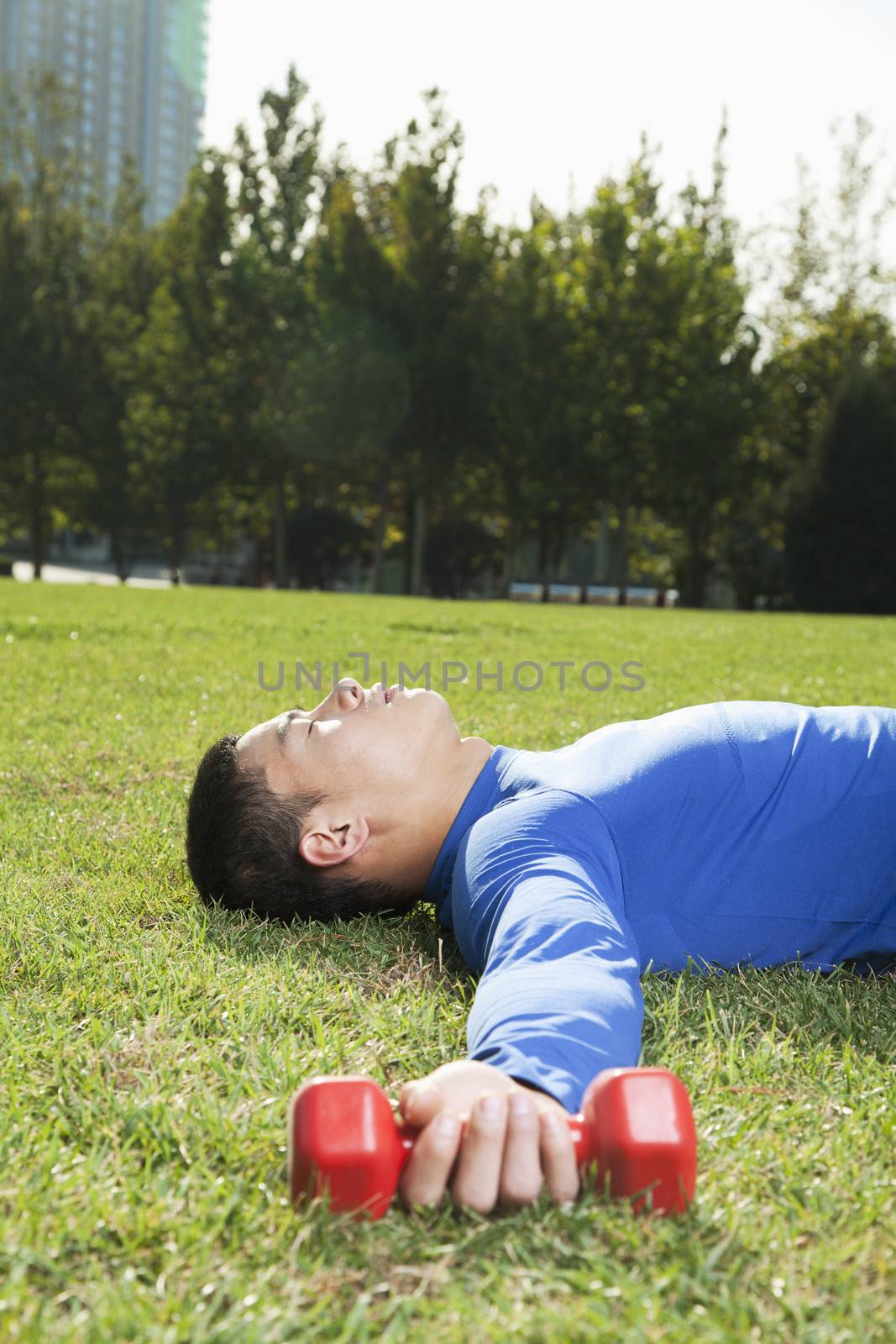 Young Athletic Man Lying Down in Park with Dumbbells, Vertical