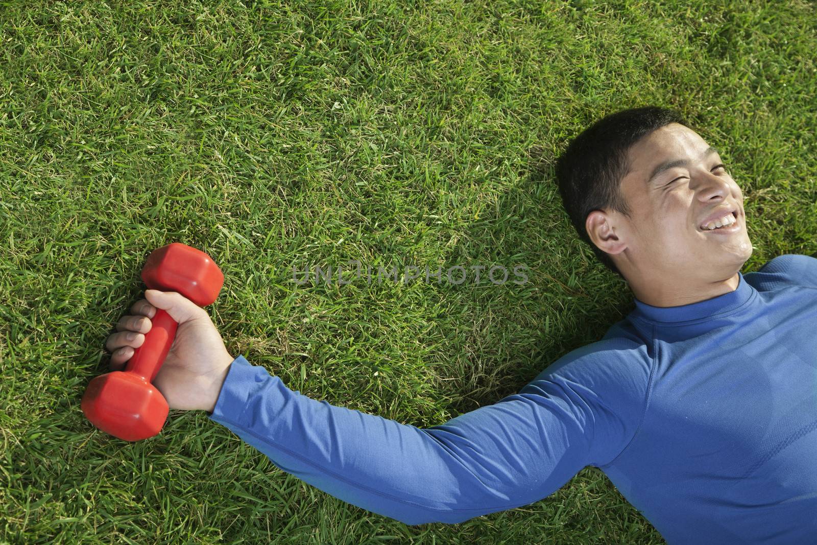 Young Athletic Man Lying Down in Grass with Dumbbells, Close Up