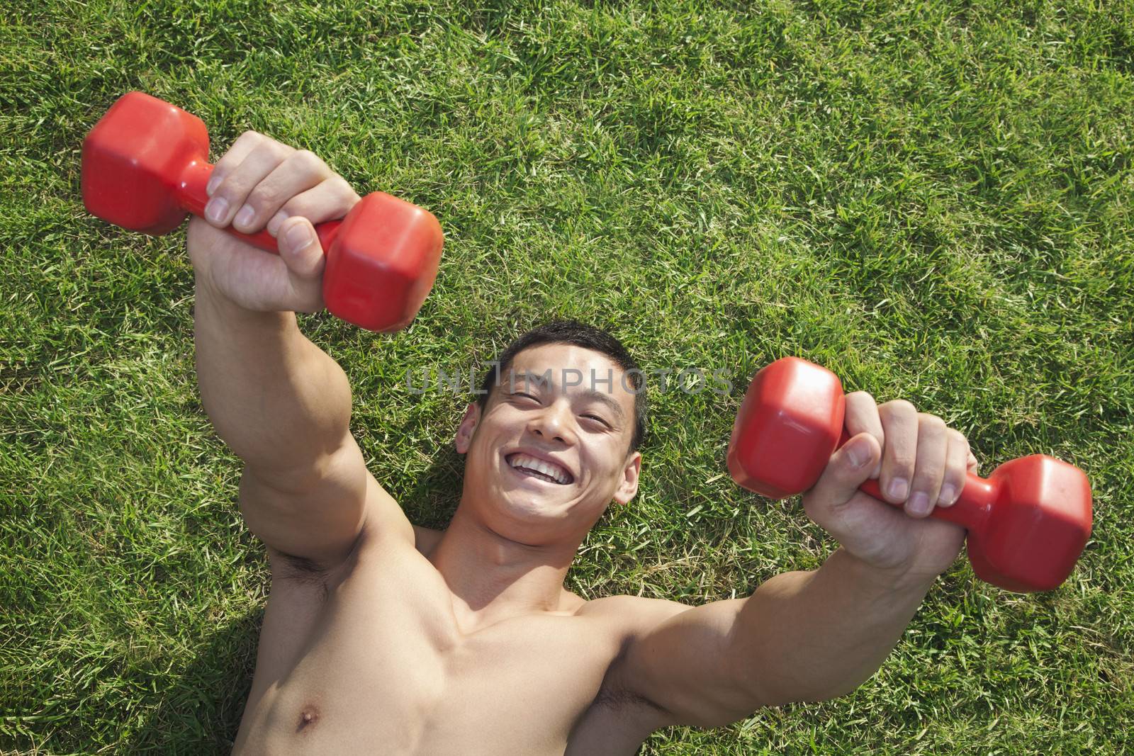 Shirtless Man Exercising with Dumbbells in Grass