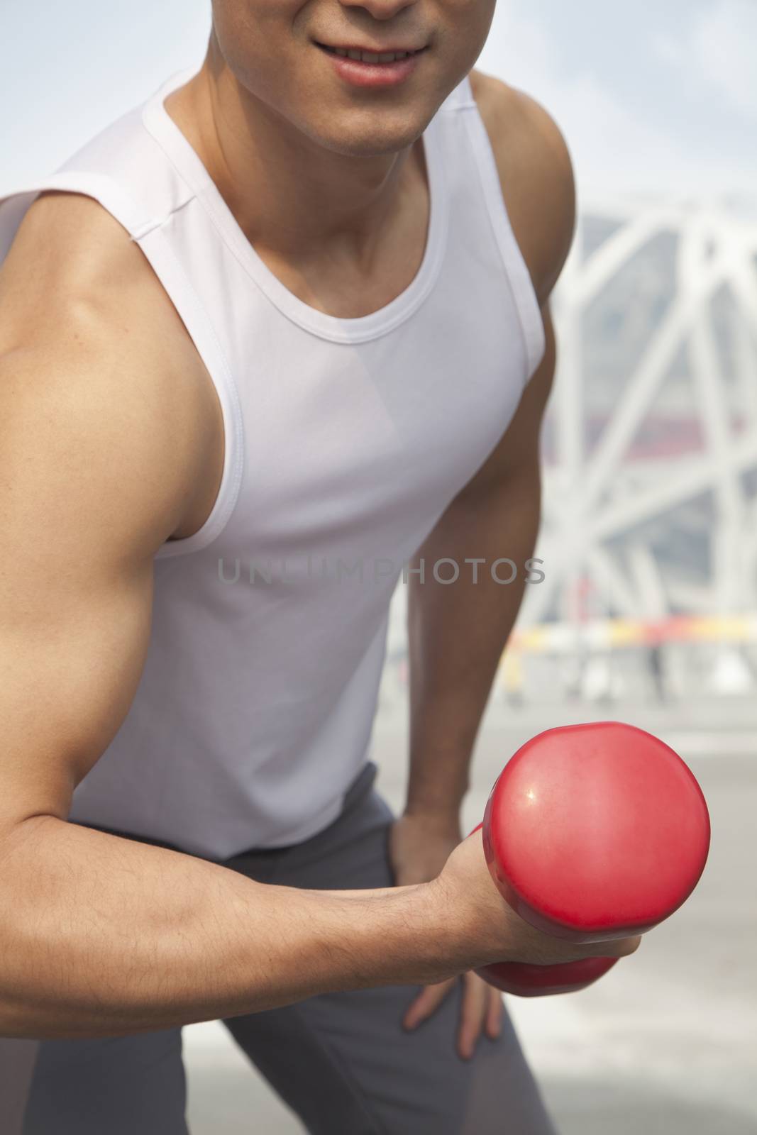 Young man exercising with dumbbell, close-up, midsection 
