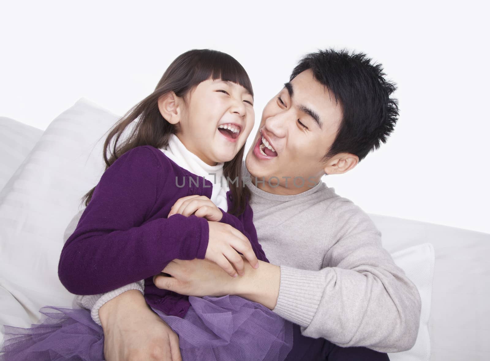 Father tickling daughter on the sofa, studio shot