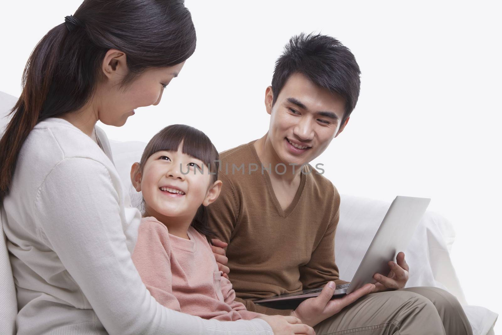 Family sitting on the sofa using laptop, mother looking at daughter, studio shot by XiXinXing