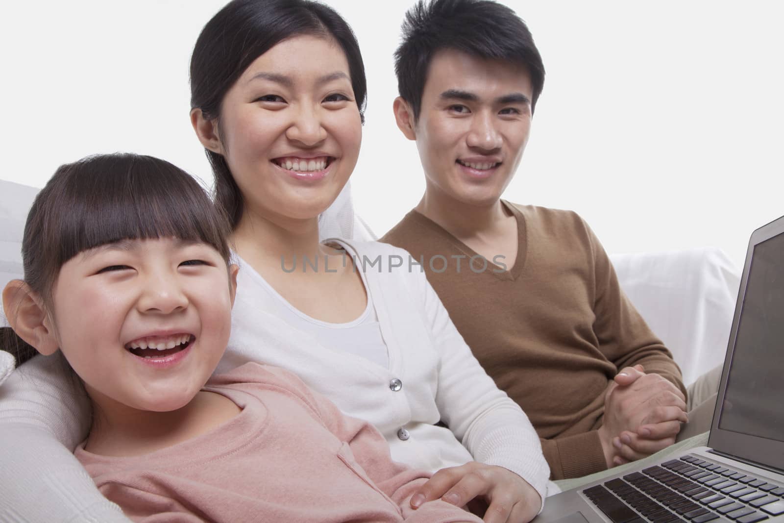 Family sitting on the sofa using laptop, looking at camera, studio shot by XiXinXing