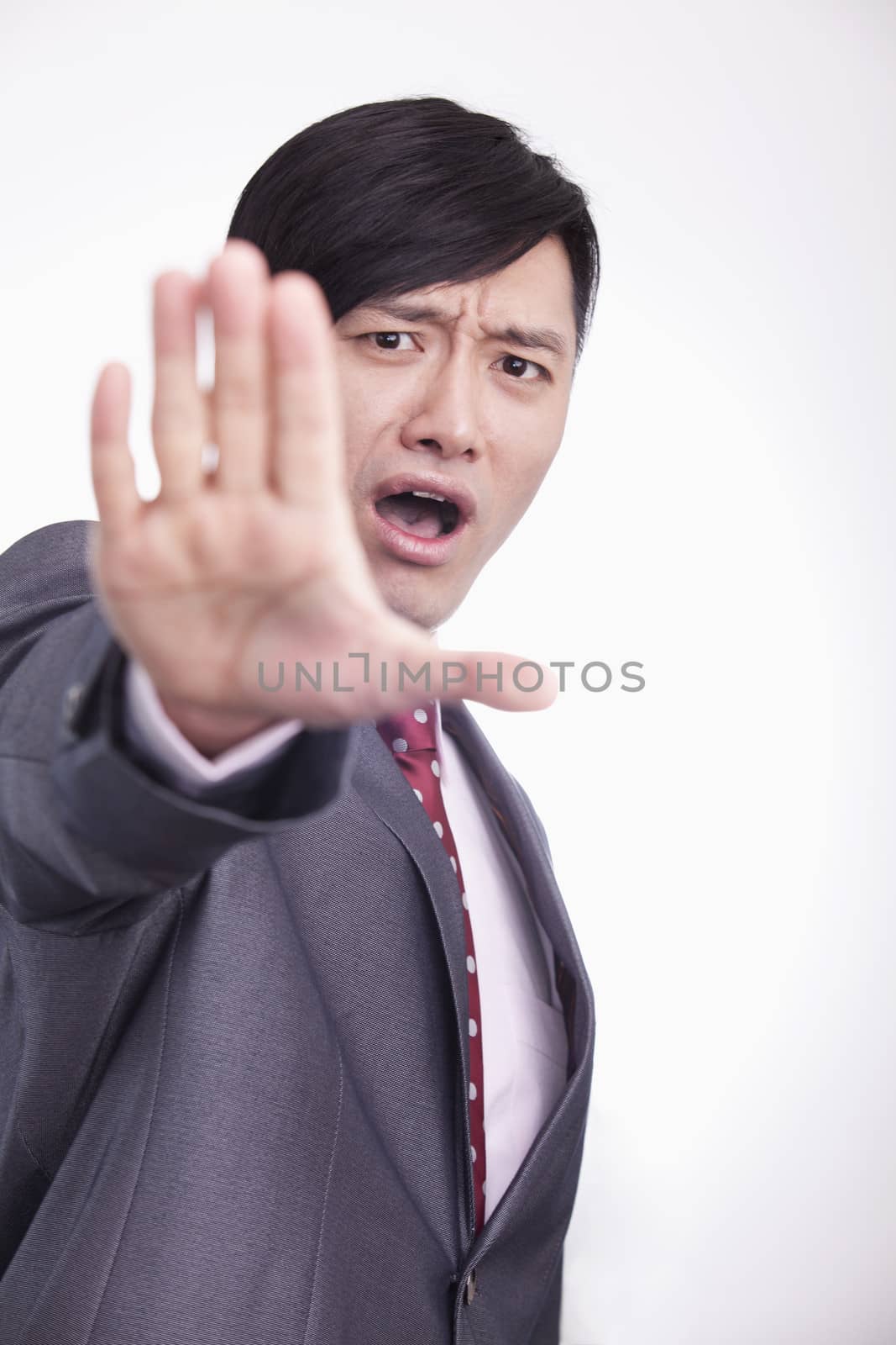 Young businessman with hand raised in stop gesture, studio shot