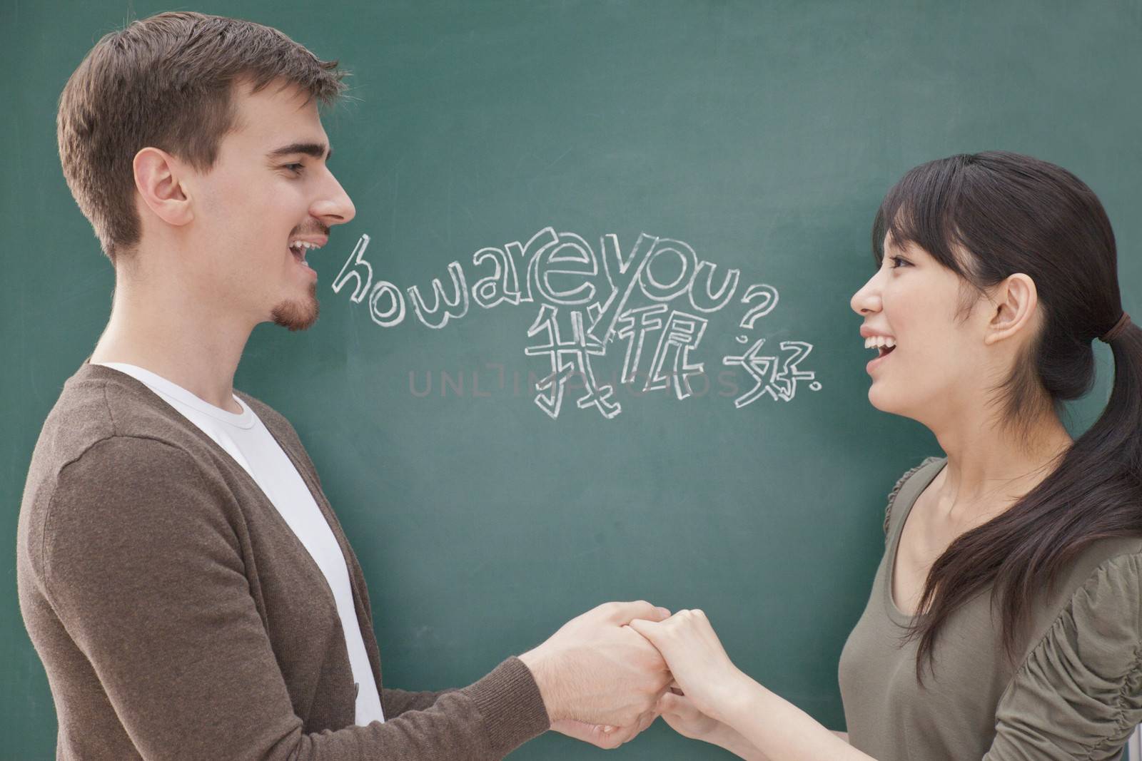 Portrait of smiling male teacher and student in front of chalkboard holding hands