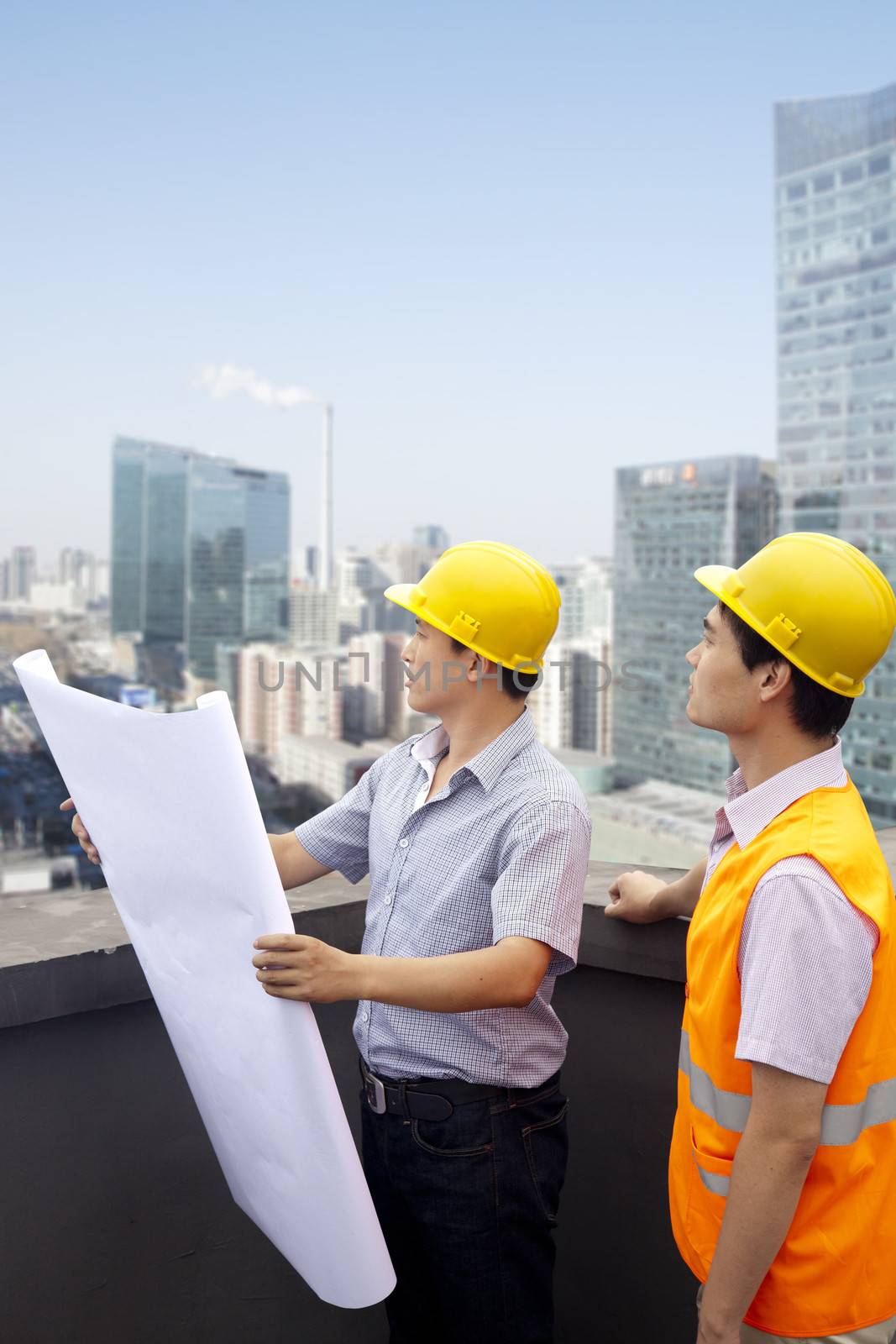 Architect And Construction Worker Talking On Rooftop