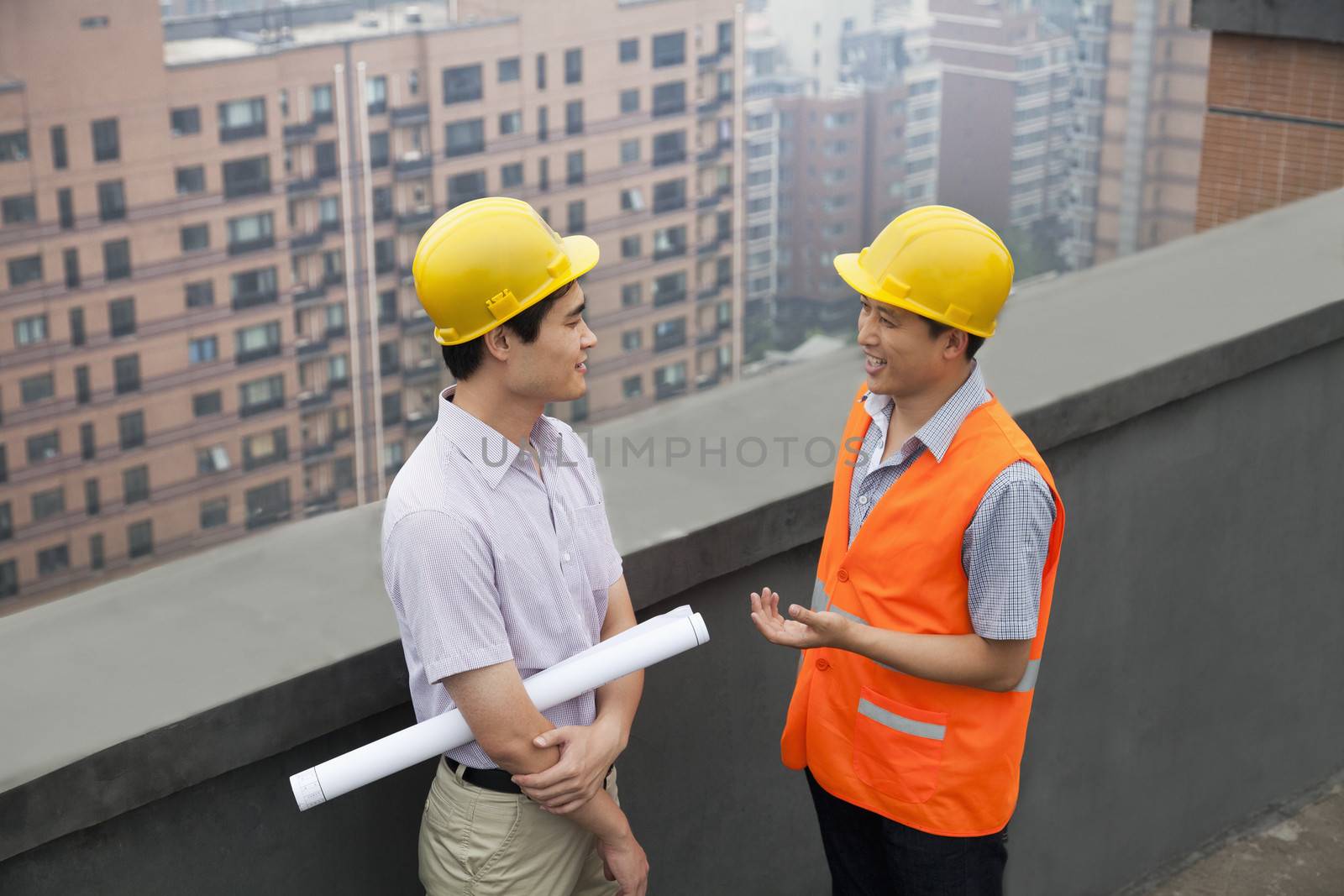 Architect And Construction Worker Talking On Rooftop