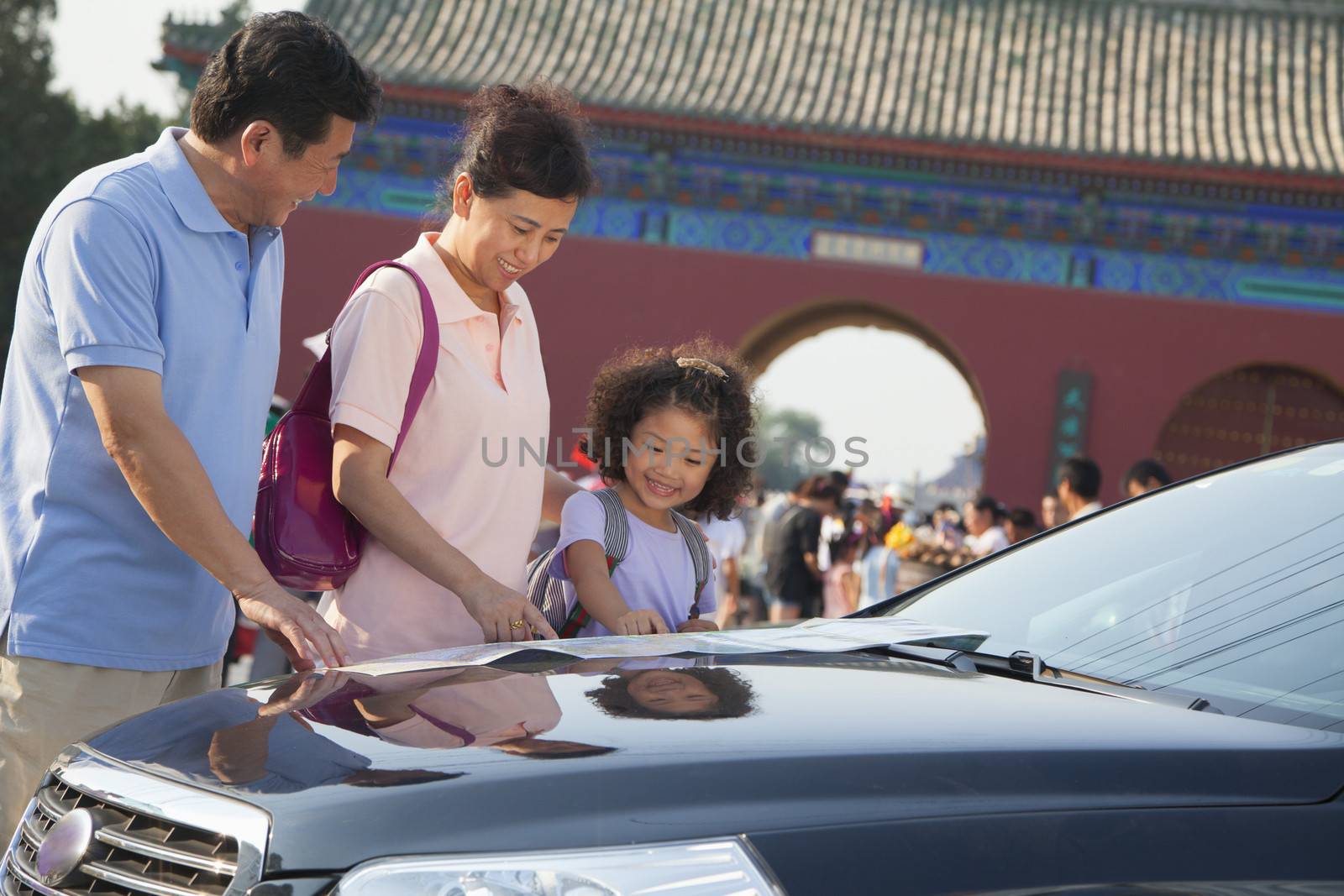 Grandparents and granddaughter standing next to the car and looking at the map