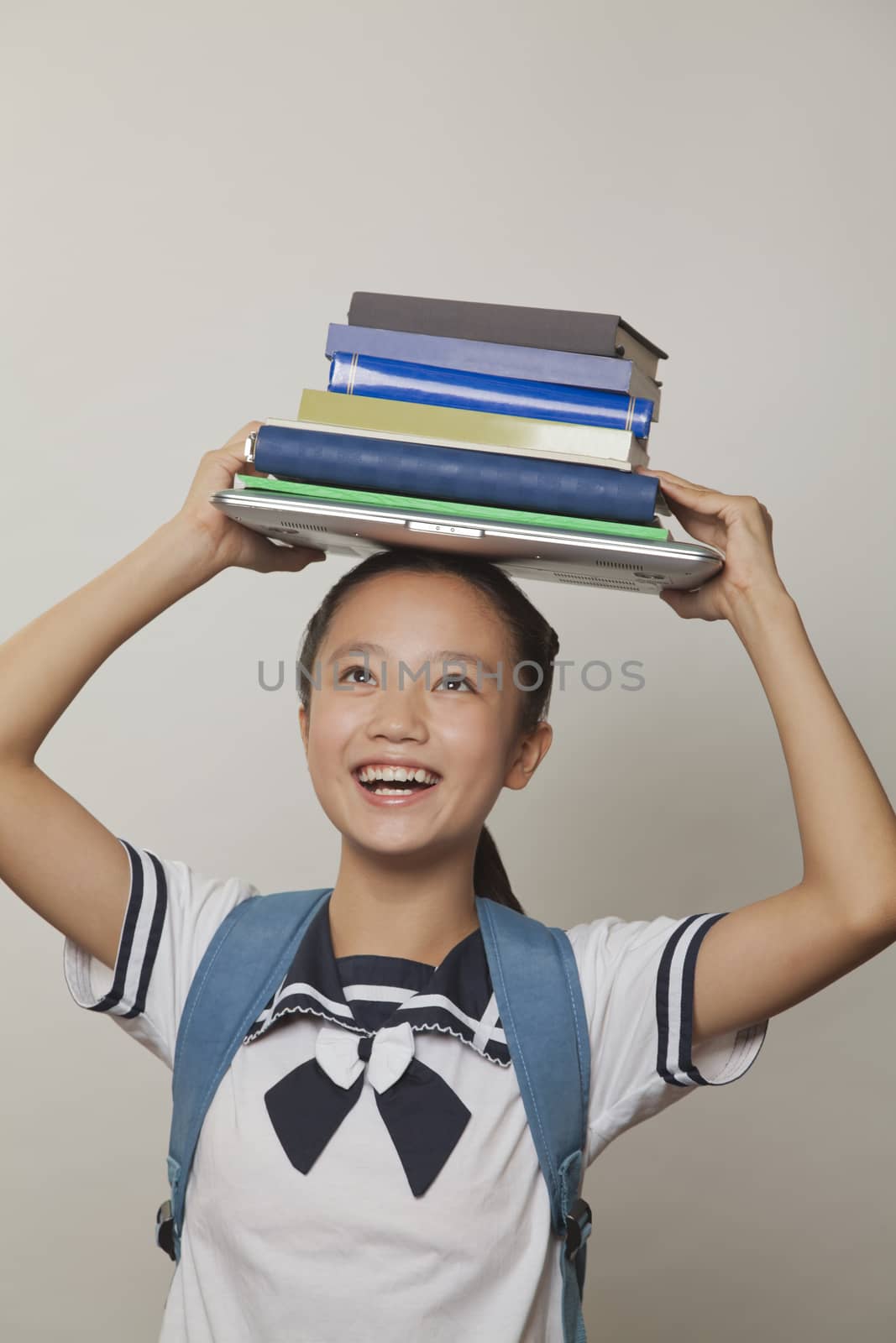 Girl smiling and holding bunch of notebooks and laptop on her head, Studio