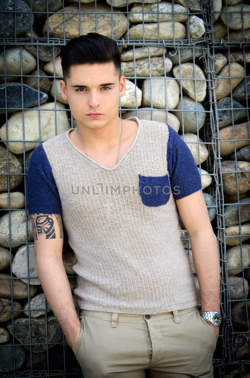 Handsome young man standing in front of stone wall, casual clothes