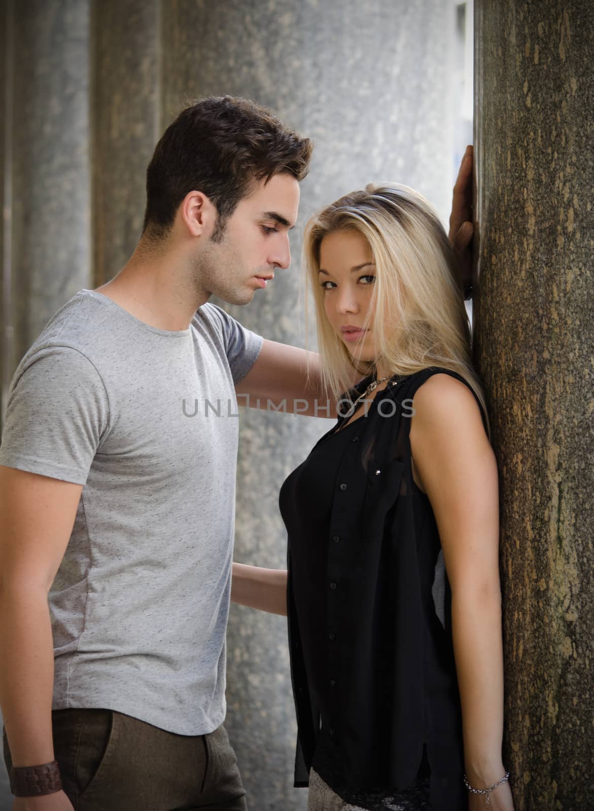 Attractive couple, young man and girl standing next to each other, marble columns behind