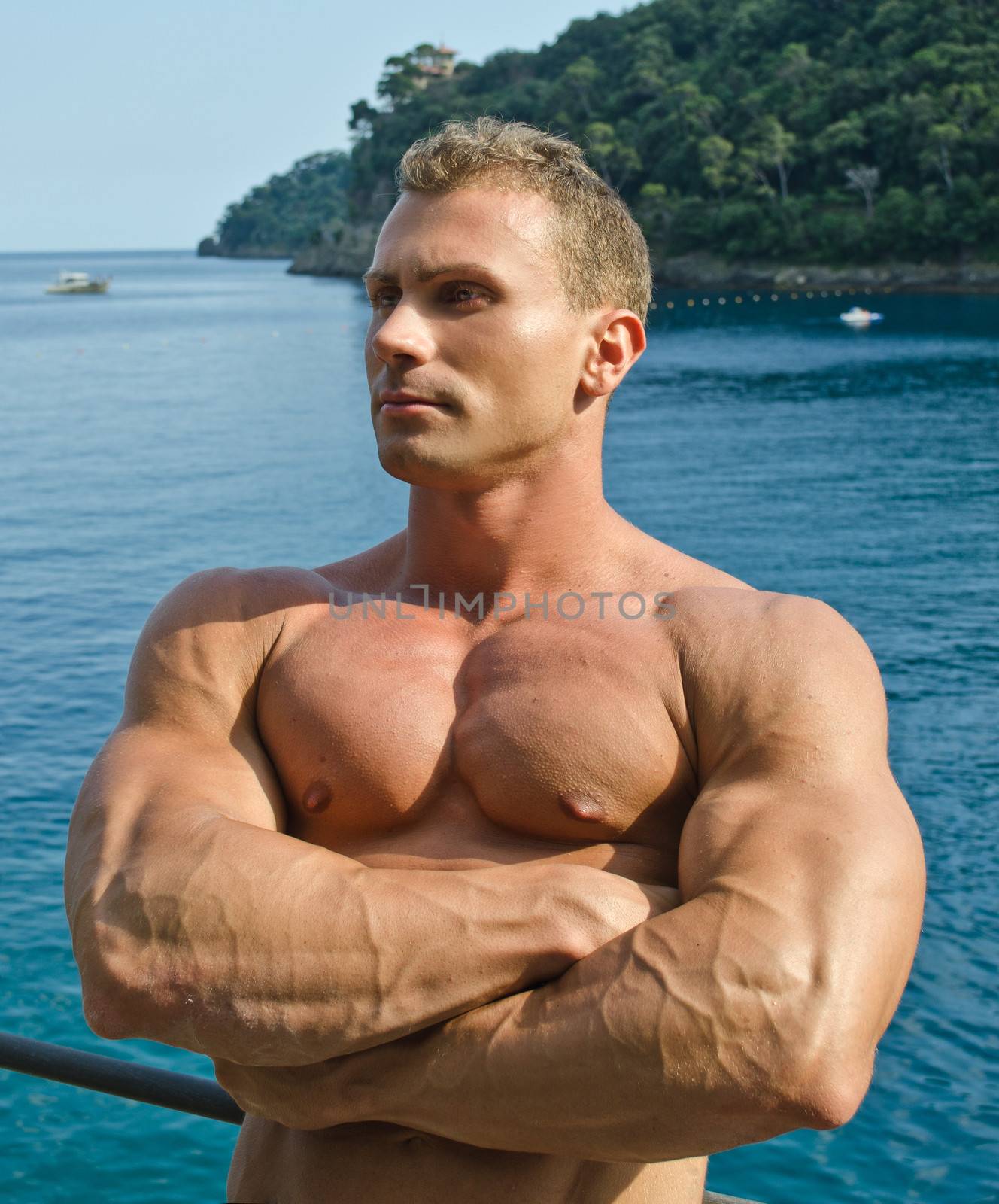 Handsome young bodybuilder, outdoors with arms crossed and the sea behind