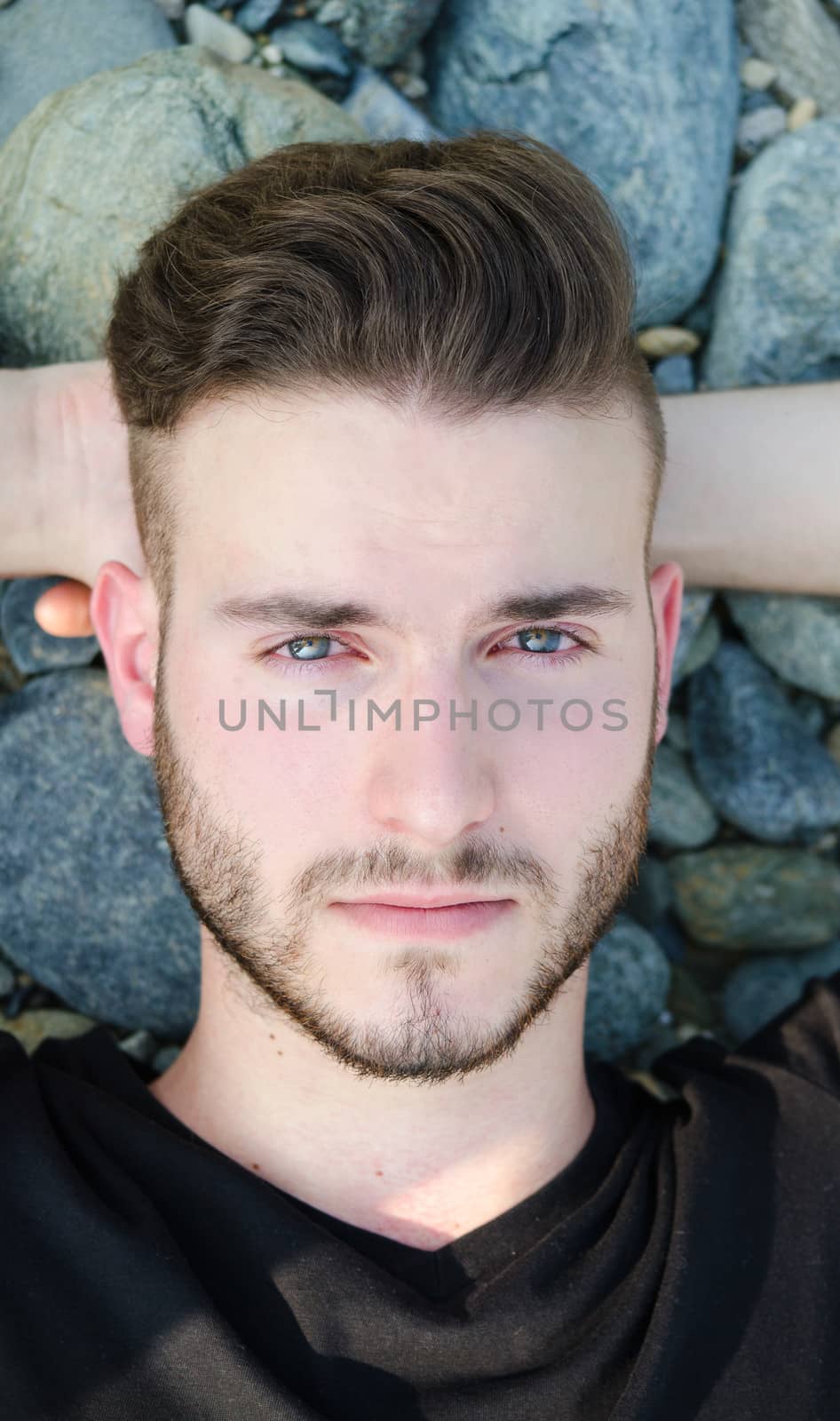 Portrait of attractive young man resting on rocks, looking in camera