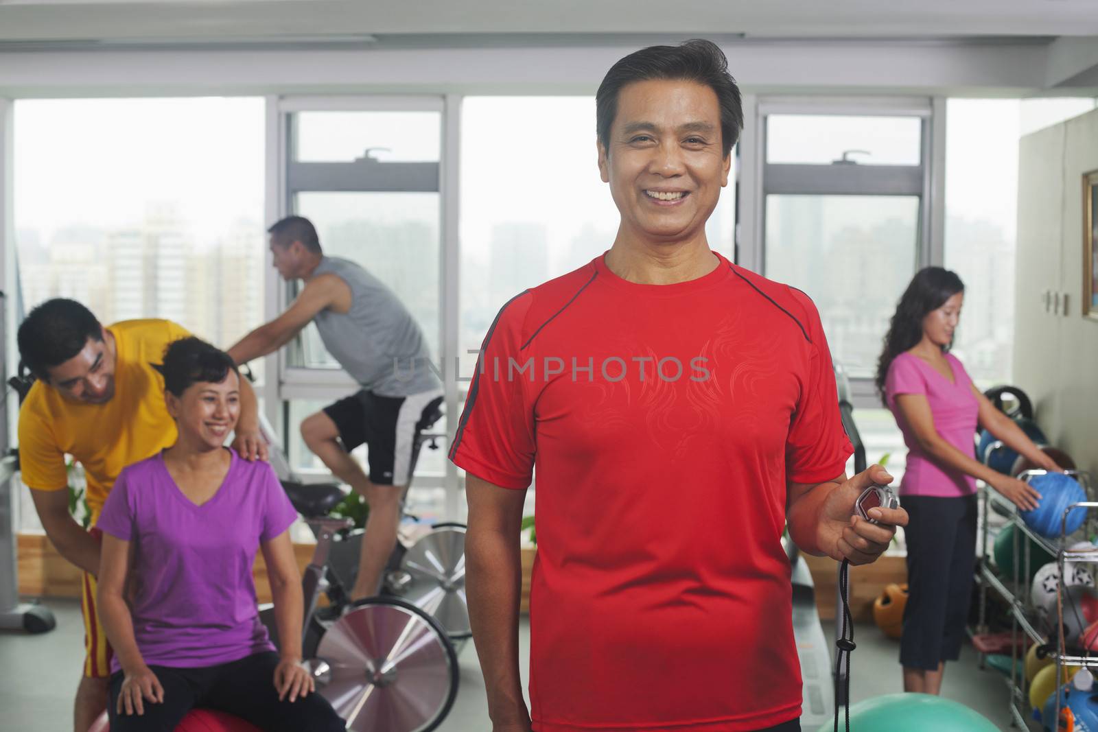 Man with stopwatch on the foreground, people working out in the gym on the background