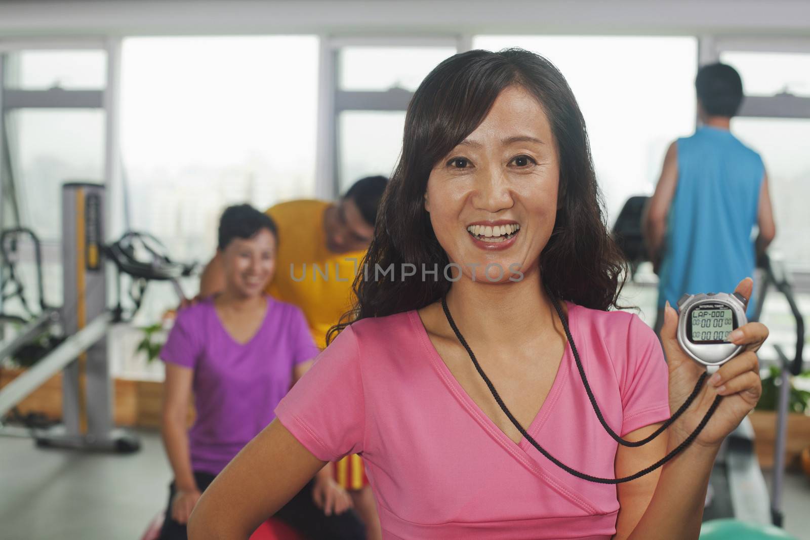 Woman holding stopwatch on foreground, people working out in the gym on the background