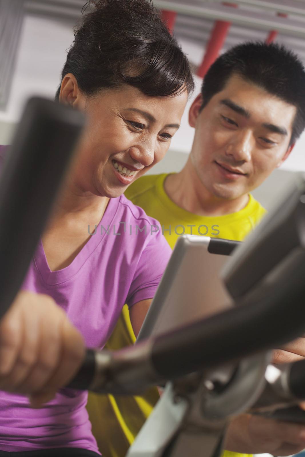 Woman smiling and exercising on the exercise bike with her trainer by XiXinXing