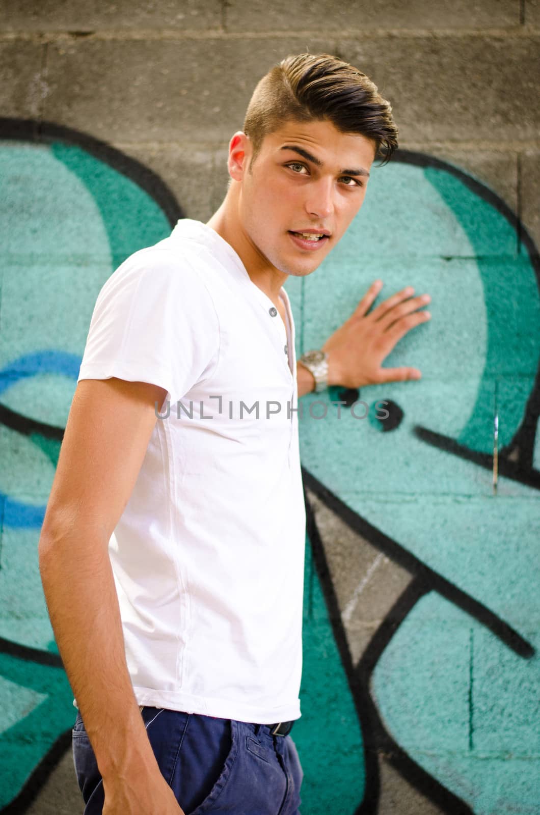 Handsome young man standing next to colorful graffiti covered wall