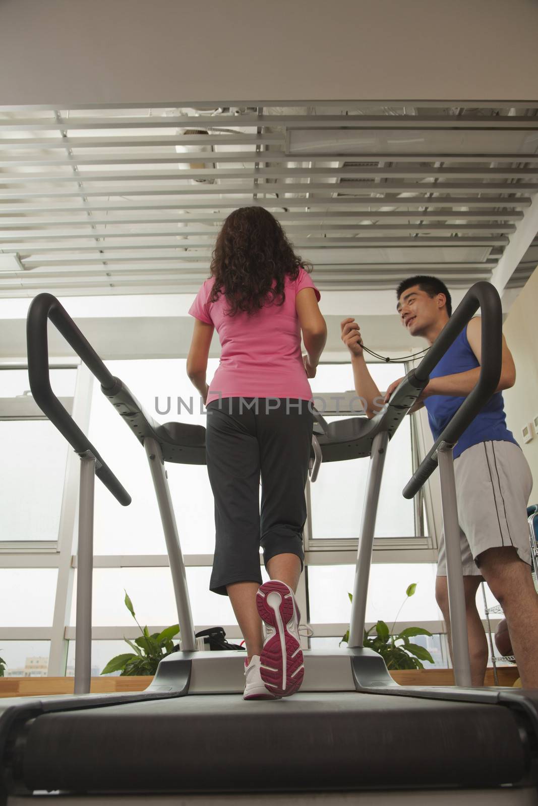 Woman walking on treadmill, trainer standing with stopwatch