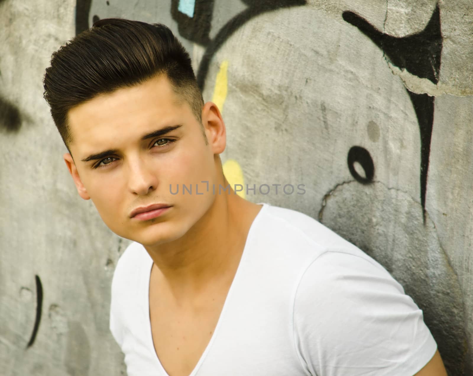 Handsome young man leaning against urban graffiti covered wall